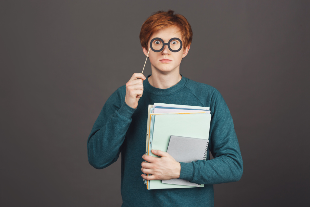 portrait-funny-handsome-redhead-teen-green-fashionable-sweater-holding-notebooks-hand-looking-with-popped-up-eyes-through-paper-glasses-stick (2).jpg